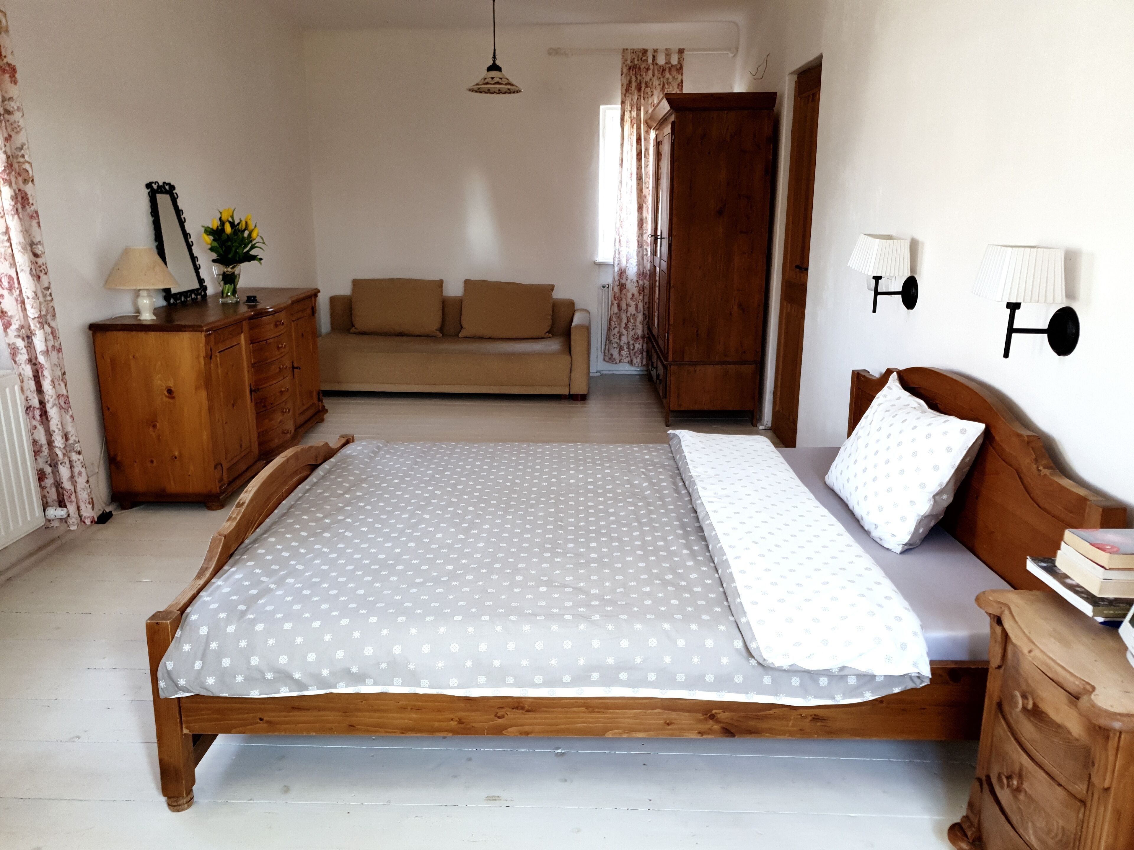 A bedroom with a wooden bed, a wooden dresser, a sofa, and a nightstand with a lamp.