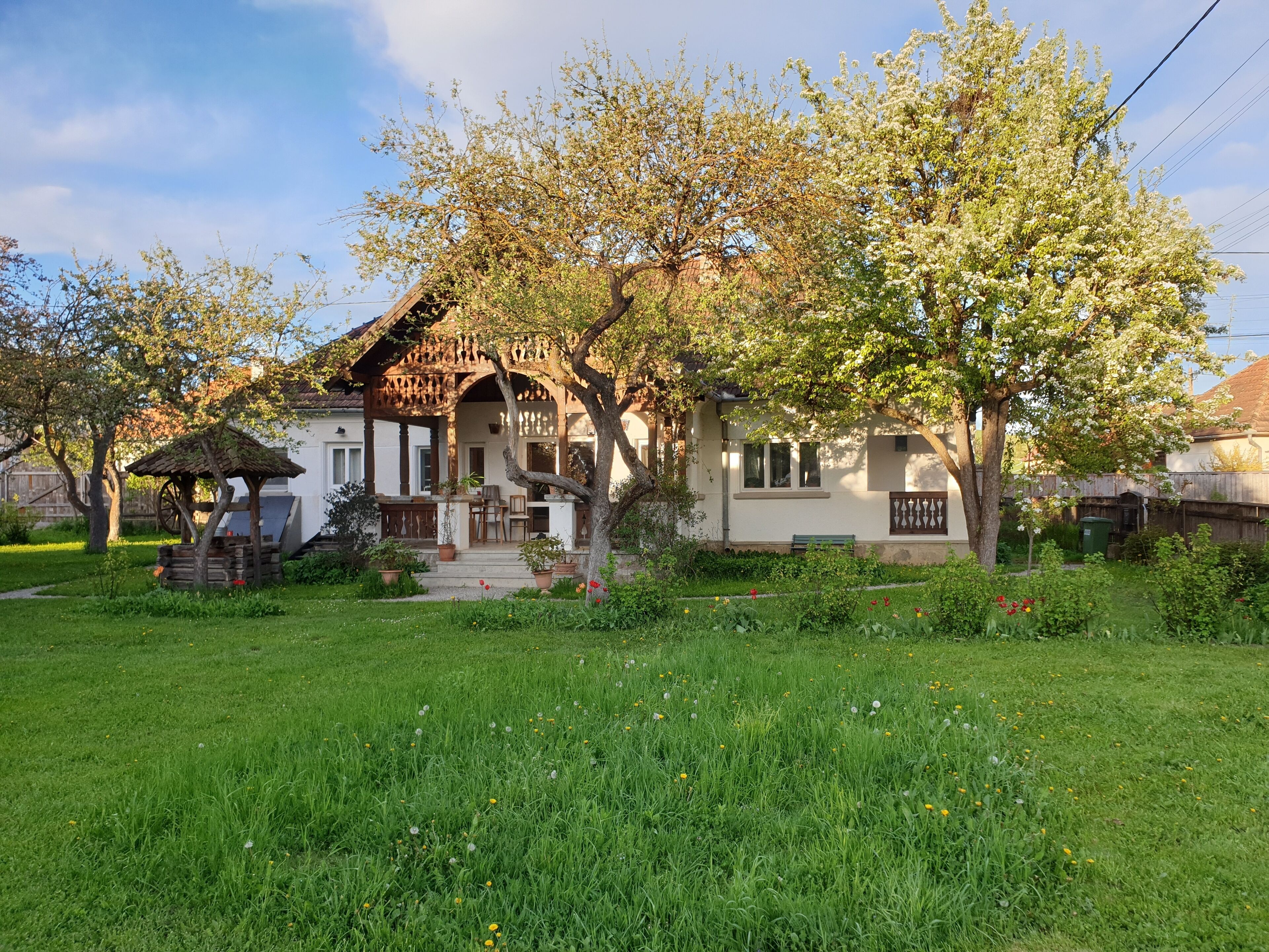 A traditional house with a wooden porch, a small garden, and a tree in front.