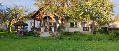A traditional house with a wooden porch, a small garden, and a tree in front.