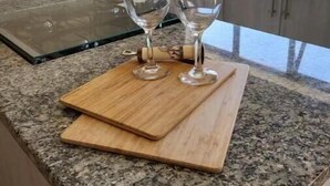 A kitchen counter with two wine glasses on a wooden board, a granite countertop, and a window with a view of trees.
