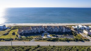 Vista aerea di un hotel sulla costa, con diversi edifici, aree di parcheggio e una strada che conduce alla spiaggia.