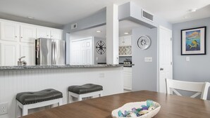 Una cucina moderna con mobili bianchi, elettrodomestici in acciaio inossidabile e un tavolo da pranzo in legno con una ciotola di oggetti decorativi.