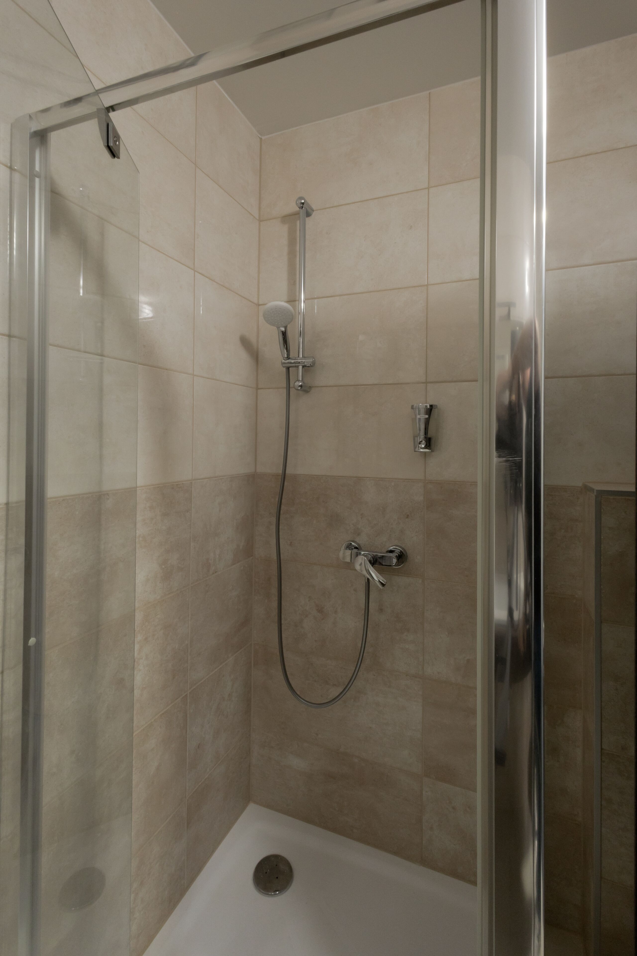 Une cabine de douche fermée par des parois en verre, dotée d’un pommeau de douche à main et d’un robinet fixé au mur.