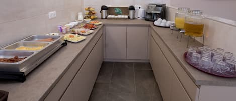 A buffet setup with various food items, coffee machines, and a beverage station.