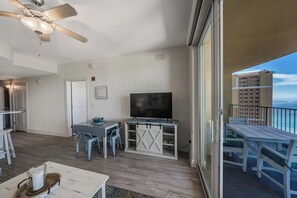 A balcony with a view of the ocean, a dining area with a table and chairs, a television, and a ceiling fan.