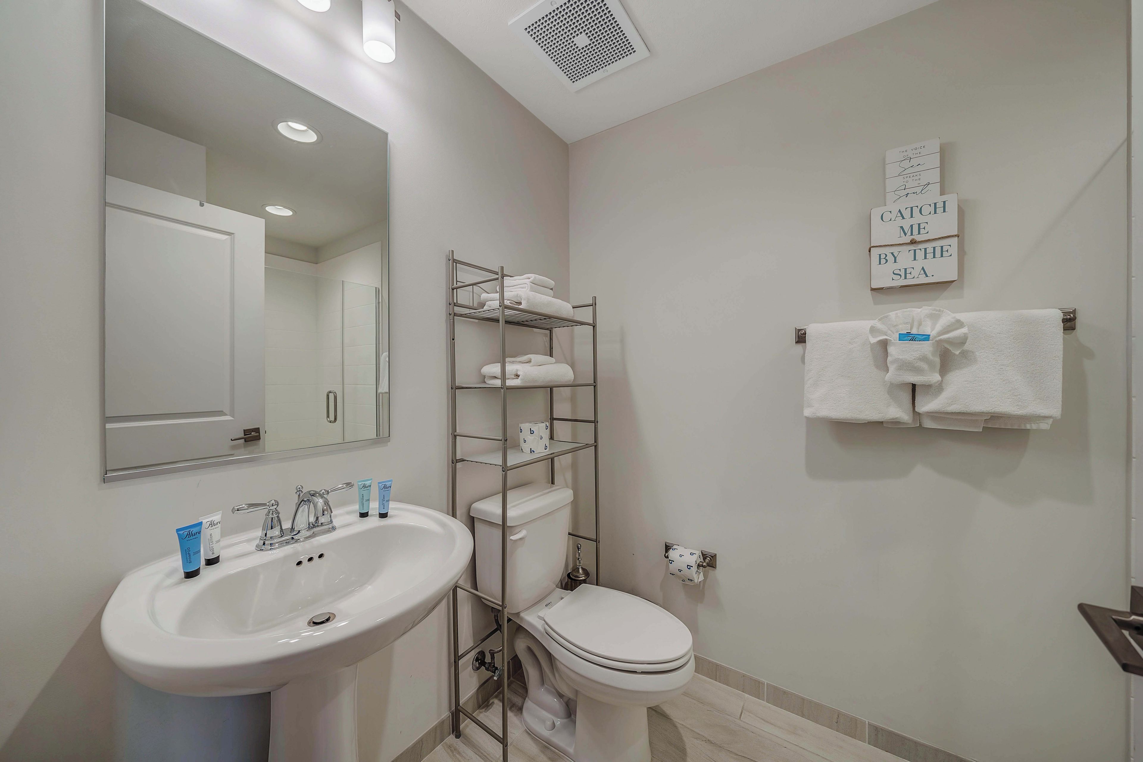 Un bagno con lavandino, specchio, WC, portasci e un cartello appeso al muro.
