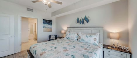 Un dormitorio con cama, mesitas de noche, ventilador de techo y una obra de arte colgada en la pared.