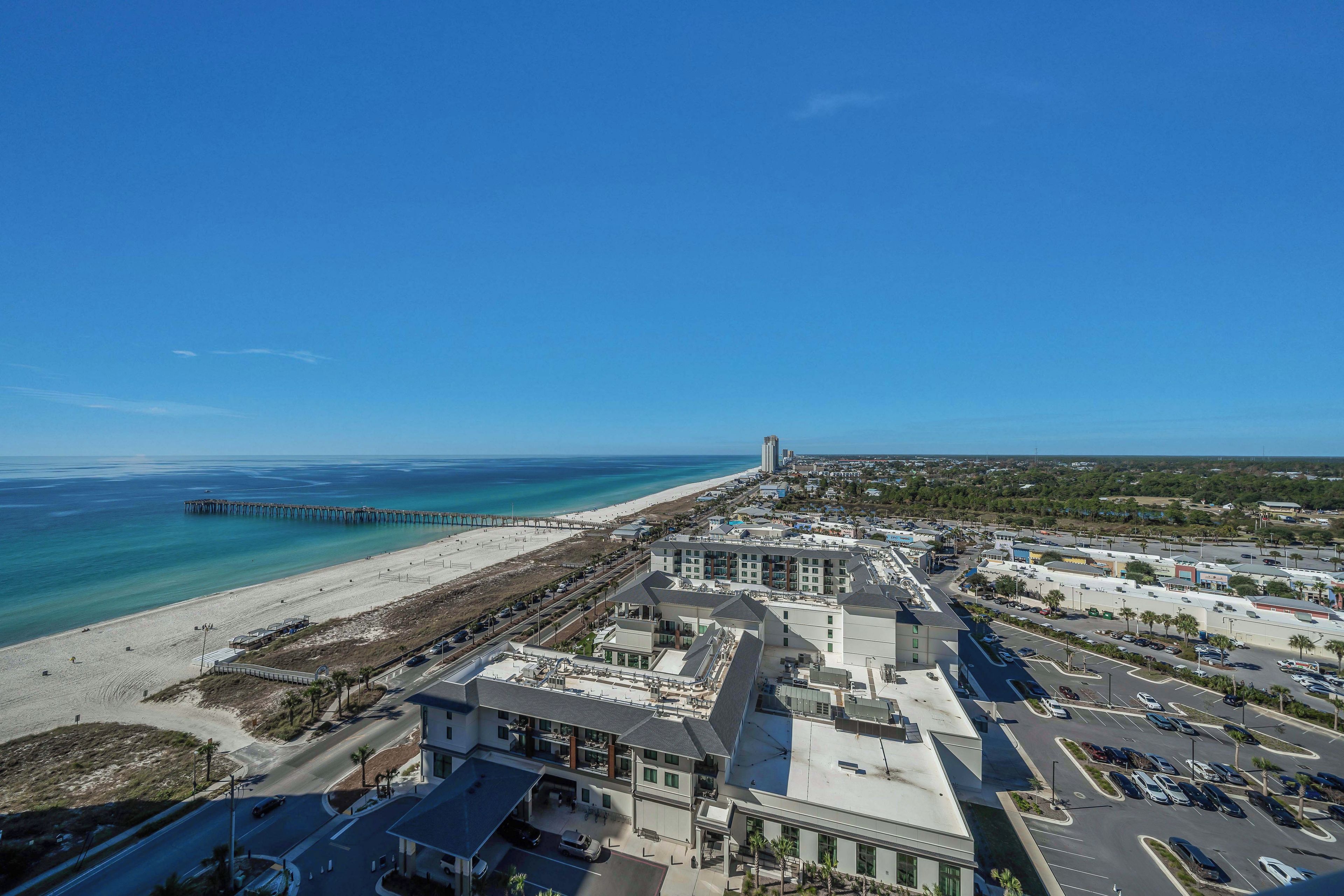 An aerial view of a coastal town with a beach, a pier, and a mix of commercial and residential buildings.