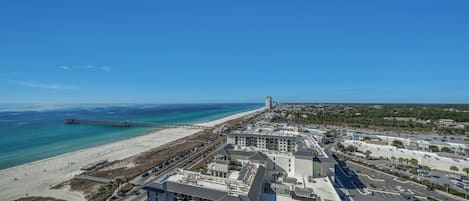 An aerial view of a coastal town with a beach, a pier, and a mix of commercial and residential buildings.