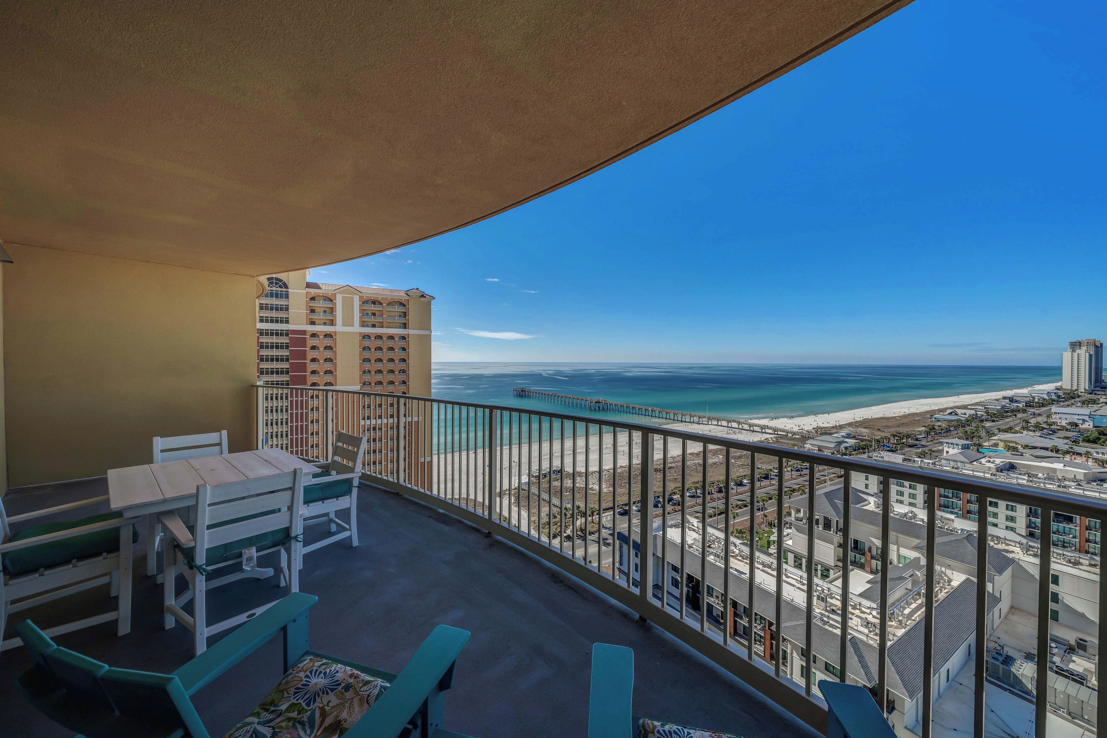 A balcony with a view of a beach and a pier, furnished with a table and chairs.