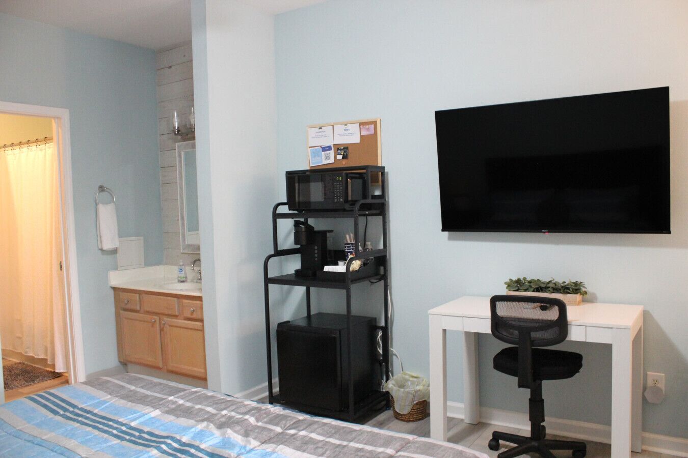 Una habitación compacta con cama, kitchenette, televisor y escritorio con silla.