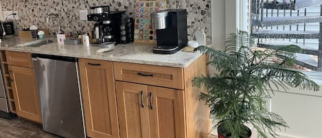 Una cocina con armarios de madera, lavavajillas de acero inoxidable, cafetera y una planta en maceta.