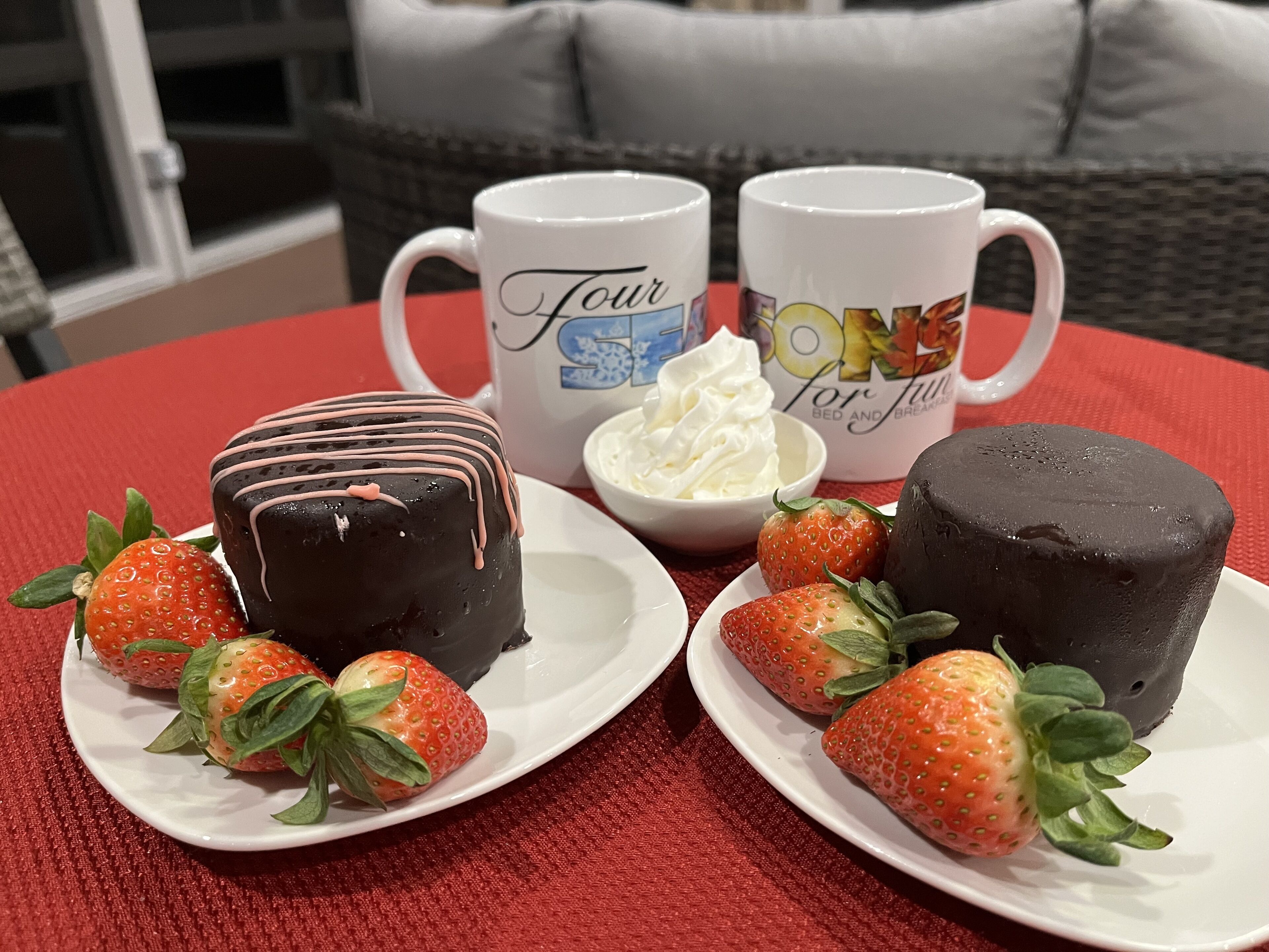 A table with two plates of strawberries and chocolate desserts, a bowl of whipped cream, and two mugs with text.