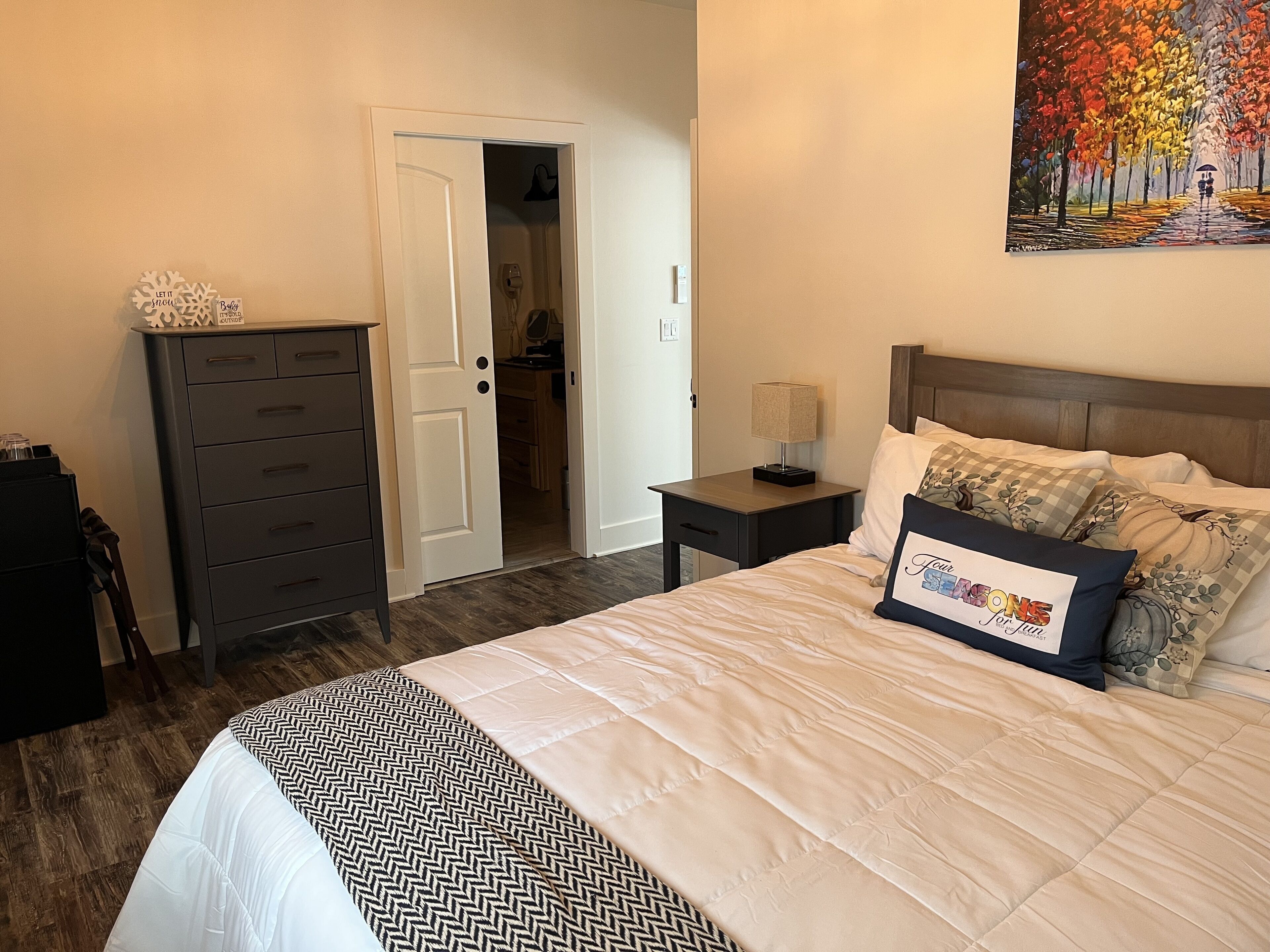 A bedroom with a bed, a nightstand, a dresser, and a door leading to a bathroom.