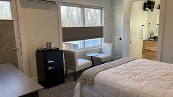 A hotel room with a bed, a desk, a chair, a small table, a wardrobe, and a window with blinds.