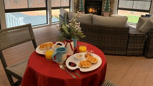 A breakfast setup with waffles, berries, and orange juice on a red table, with a fireplace and wicker furniture in the background. - Four Seasons For Fun (Lakeville)