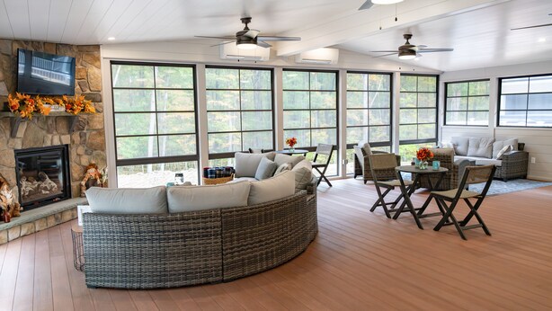 A spacious living room with a stone fireplace, large windows, wicker furniture, and ceiling fans. - Four Seasons For Fun (Lakeville)