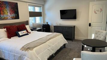 A bedroom with a bed, a desk, a chair, a TV, and a door.