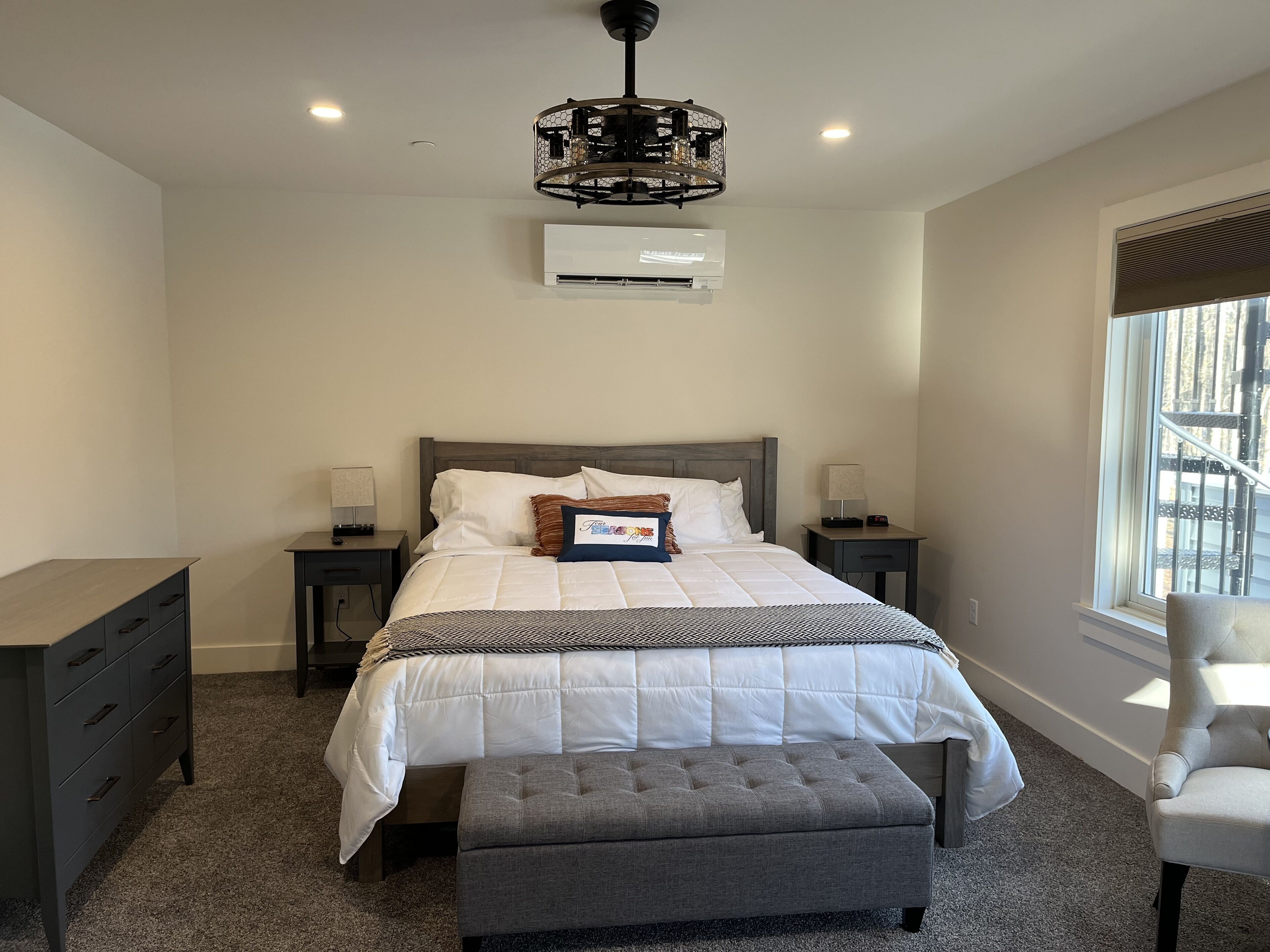 Quarto com cama, mesas de cabeceira, ar condicionado, janela com vista e uma cadeira.