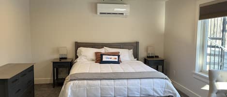 Ein Schlafzimmer mit einem Bett, Nachttischen, einer Klimaanlage, einem Fenster mit Aussicht und einem Sessel.