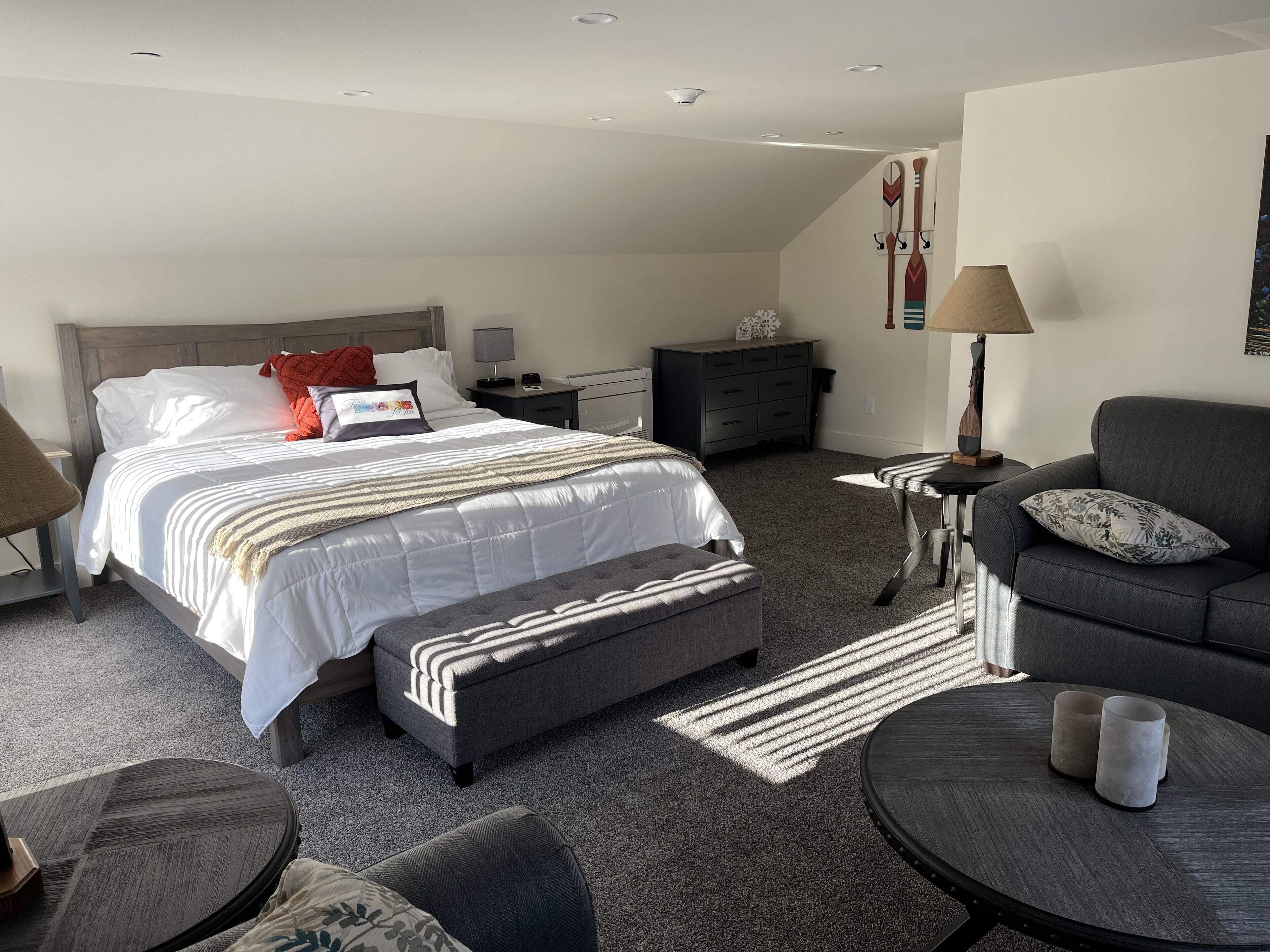 Ein modernes Schlafzimmer mit einem großen Bett, einem grauen Sofa, einem runden Couchtisch und einem kleinen Beistelltisch.