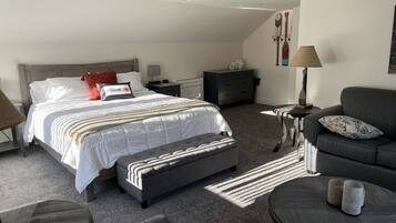 Ein modernes Schlafzimmer mit einem großen Bett, einem grauen Sofa, einem runden Couchtisch und einem kleinen Beistelltisch.