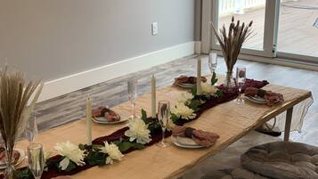 Mesa de comedor decorada con flores blancas, velas y cristalería, con vista a una terraza de madera.