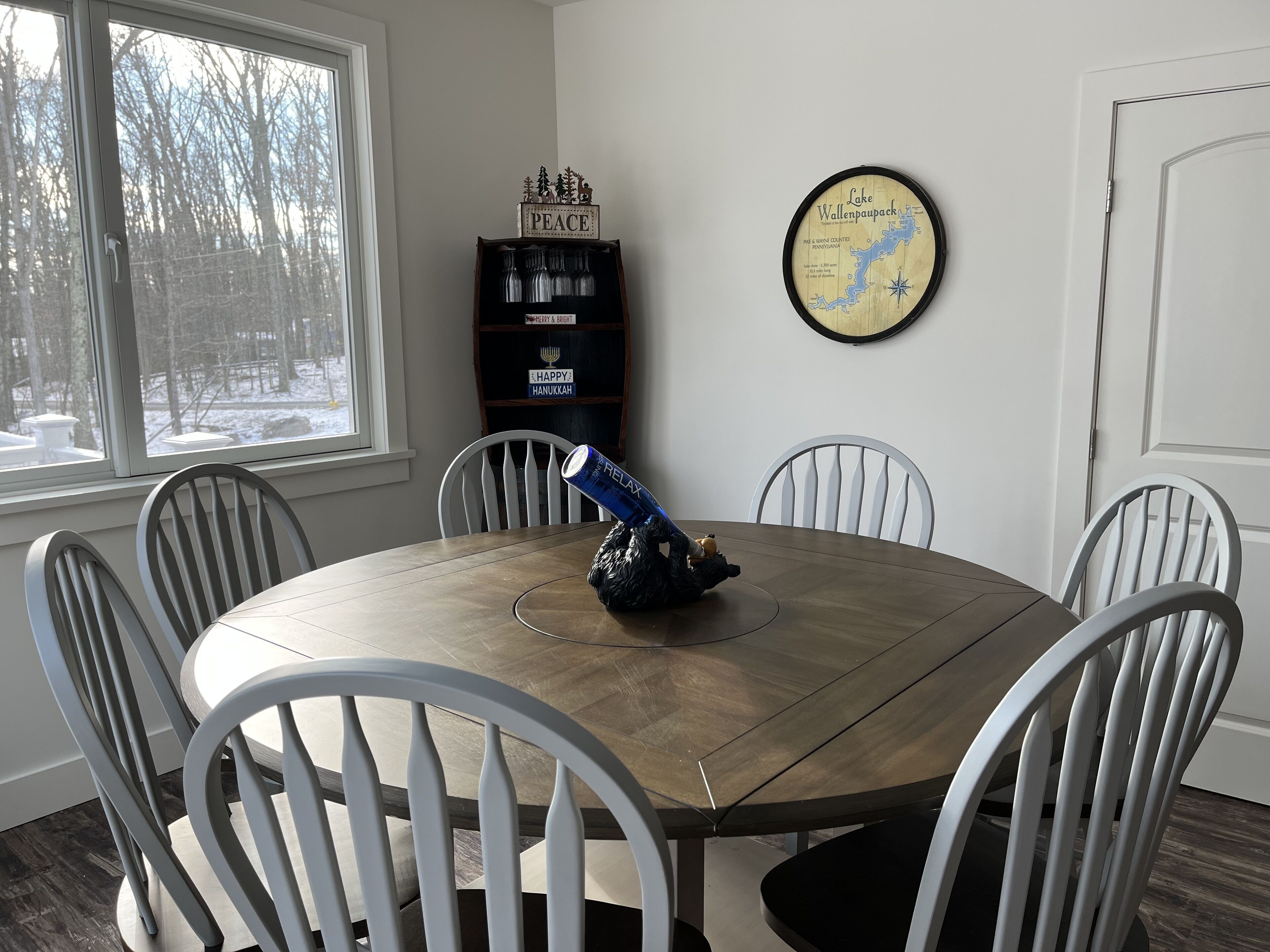A dining room with a round table, six chairs, a clock, and a bookshelf.