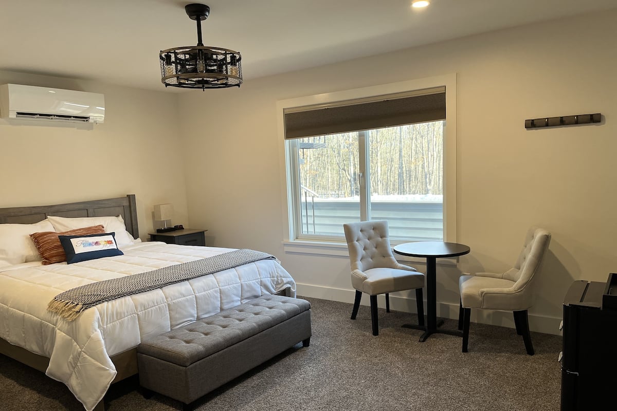 Une chambre à coucher avec un lit, une table de chevet, une lampe et une fenêtre donnant sur des arbres.