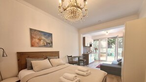 A bedroom with a bed, a desk, and a chair. There is a chandelier above the bed and a painting on the wall. - Terrace Suite - KindStay Suites Prague Airport (Stredoceský kraj)