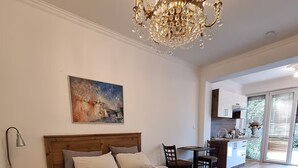 A bedroom with a large bed, a chandelier, a painting, and a view of the kitchen and outside. - Terrace Suite - KindStay Suites Prague Airport (Stredoceský kraj)