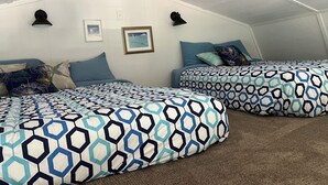 A bedroom with two beds, each with a patterned bedspread, a wall-mounted light fixture, and a framed picture.