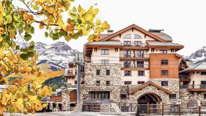 A multi-story hotel with stone and wood exterior, balconies, and a view of snow-capped mountains.