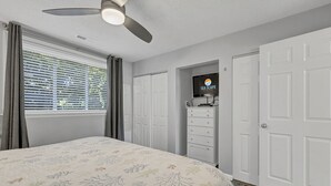 Une chambre à coucher avec un lit, un ventilateur de plafond, une télévision et une armoire.