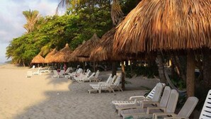 A beach with thatched-roof huts and white lounge chairs. - Home at the beach!  (Jutiapa)