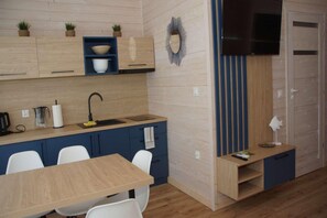 A compact kitchen with a sink, a kettle, and a coffee maker. There is a dining table with chairs and a small seating area with a bench. - Air-conditioned holiday homes, 2 bedrooms (Mielenko)