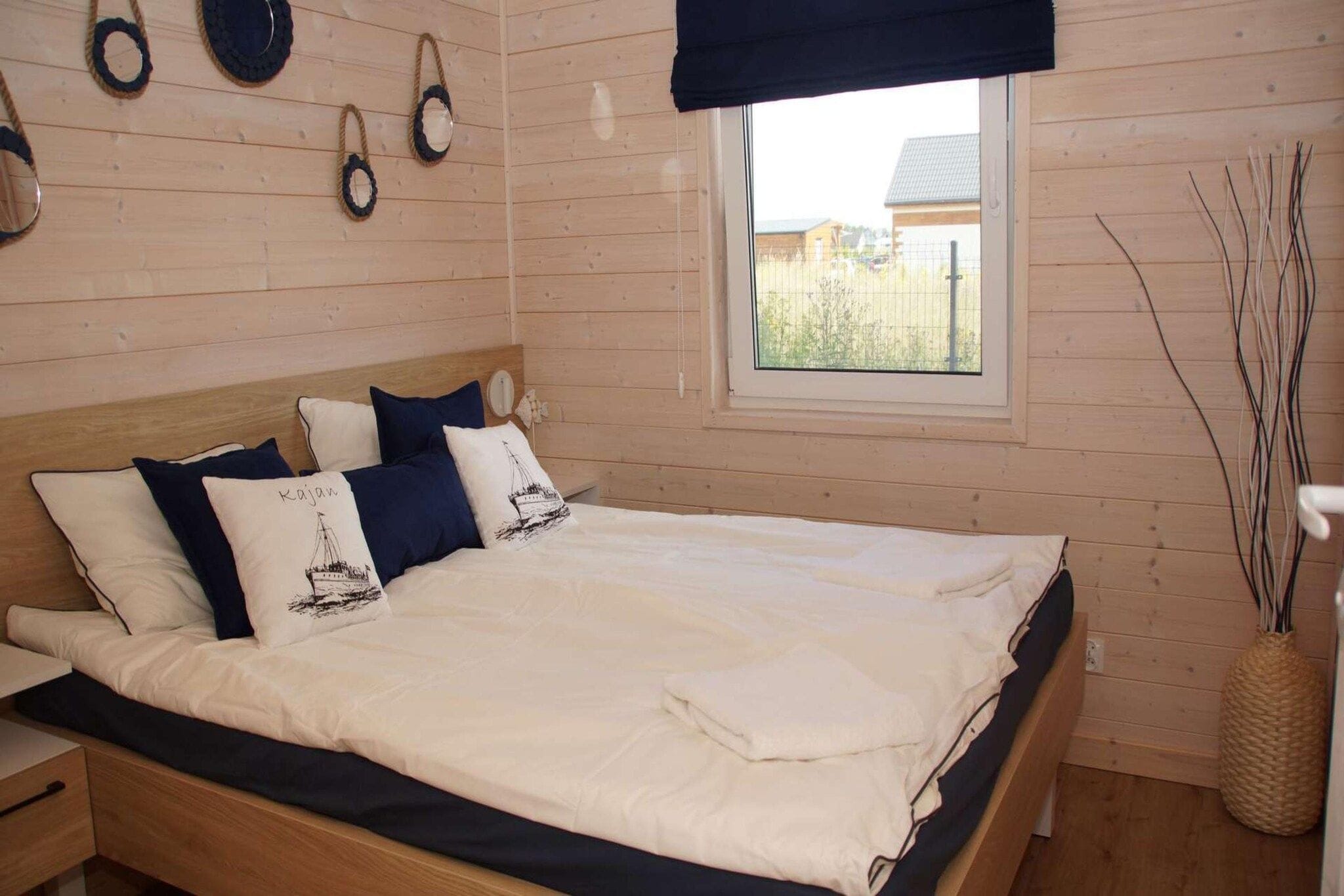 A bedroom with a bed, pillows, a window, and a wall-mounted light fixture.