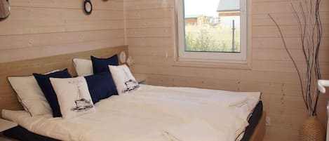 A bedroom with a bed, pillows, a window, and a wall-mounted light fixture.