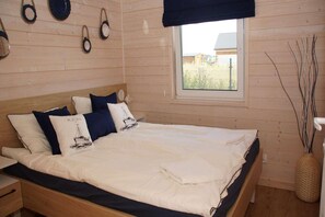A bedroom with a bed, pillows, a window, and a wall-mounted light fixture.