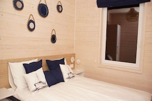 A bed with white bedding and navy pillows, a wooden headboard, a window with a view, and wall-mounted circular mirrors.