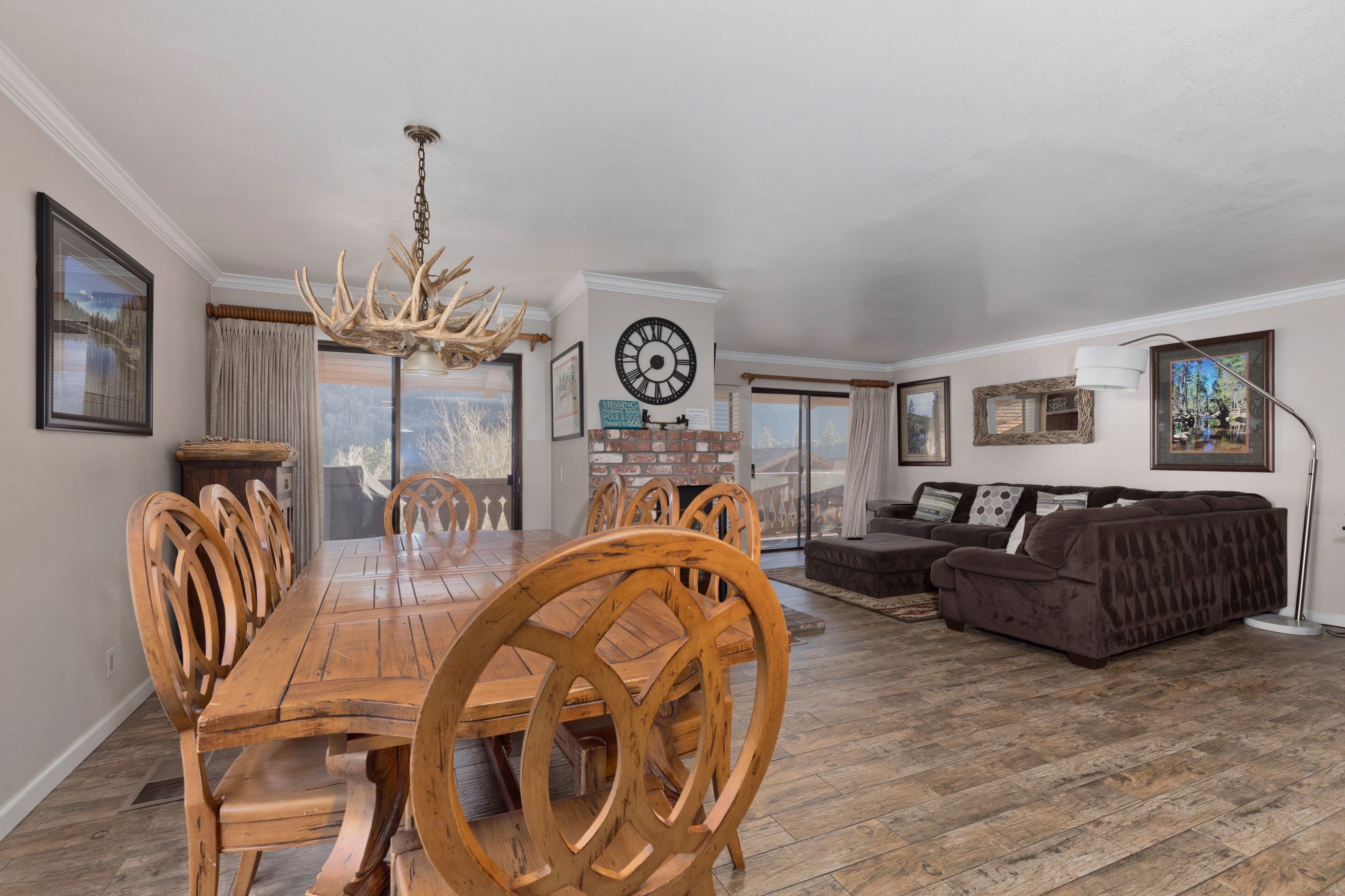 A spacious living room with a wooden dining table and chairs, a brown sofa, and a chandelier.