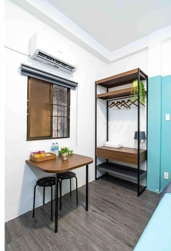 Compact room with a desk, chair, and window, featuring a functional layout and a wall-mounted air conditioning unit.
