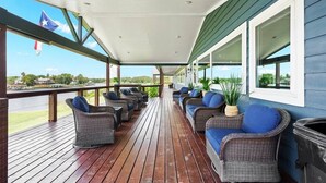 Un espace extérieur abrité, aménagé avec des meubles en osier et offrant une vue sur un terrain de golf.