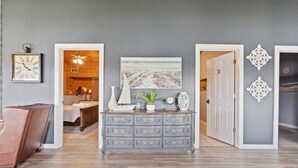 Une pièce avec un mur gris, un plancher en bois, une commode grise dotée de nombreux tiroirs, une horloge encadrée et un tableau représentant une scène de plage.