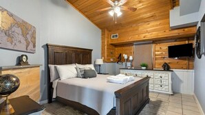 Une chambre avec un plafond en bois, un lit avec une literie blanche, une table de chevet, une commode, un téléviseur et une carte du monde accrochée au mur.