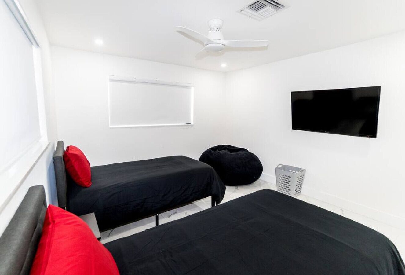 A room with two beds, a ceiling fan, a TV, and a whiteboard.