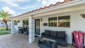 A covered patio area with outdoor furniture, including a sofa and chairs, and a small table. - Modern Luxury, 2 Mi From Beach! (Fort Lauderdale)