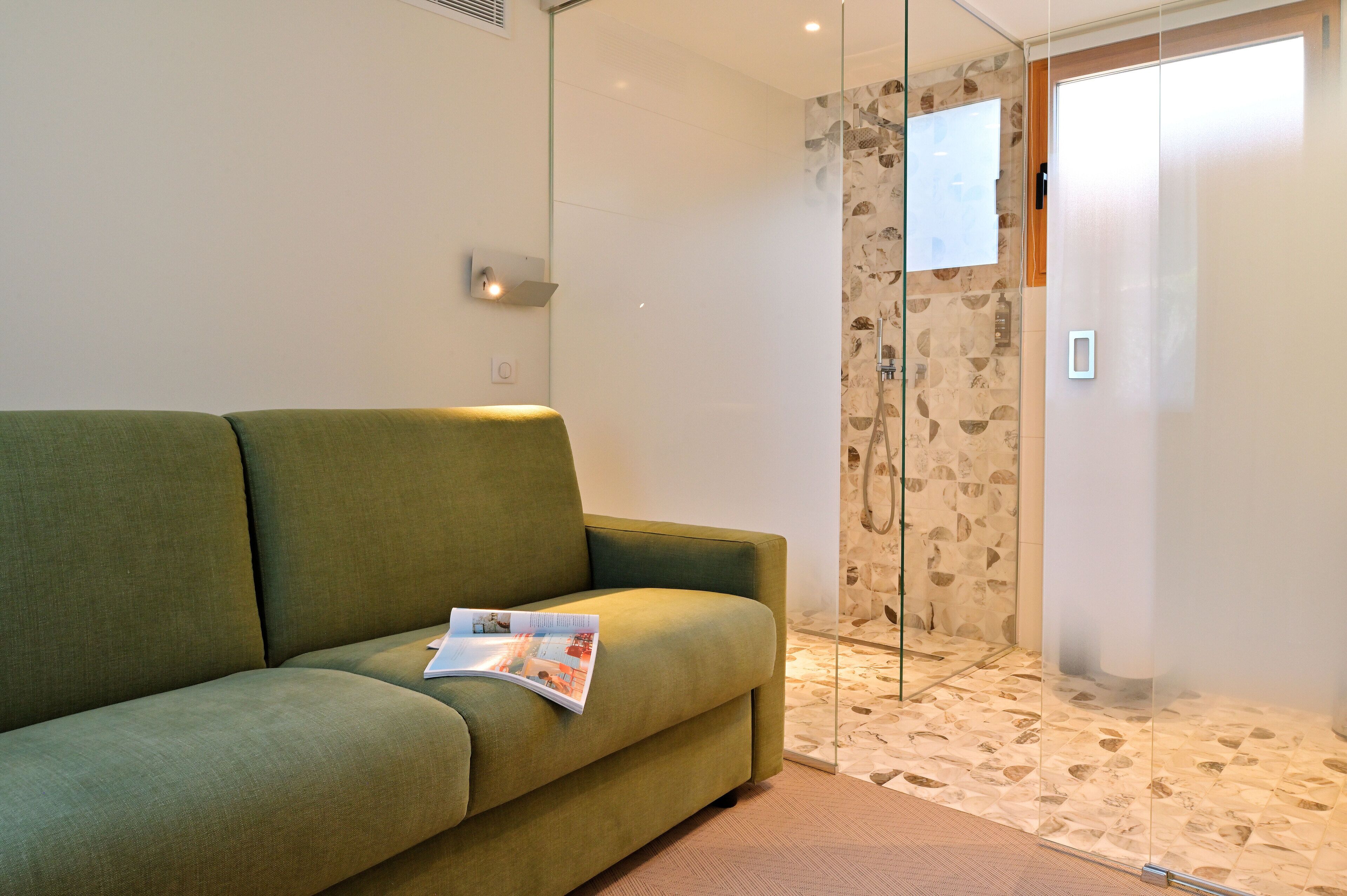 Un canapé vert avec un magazine, une cabine de douche en verre et un sol à motifs.
