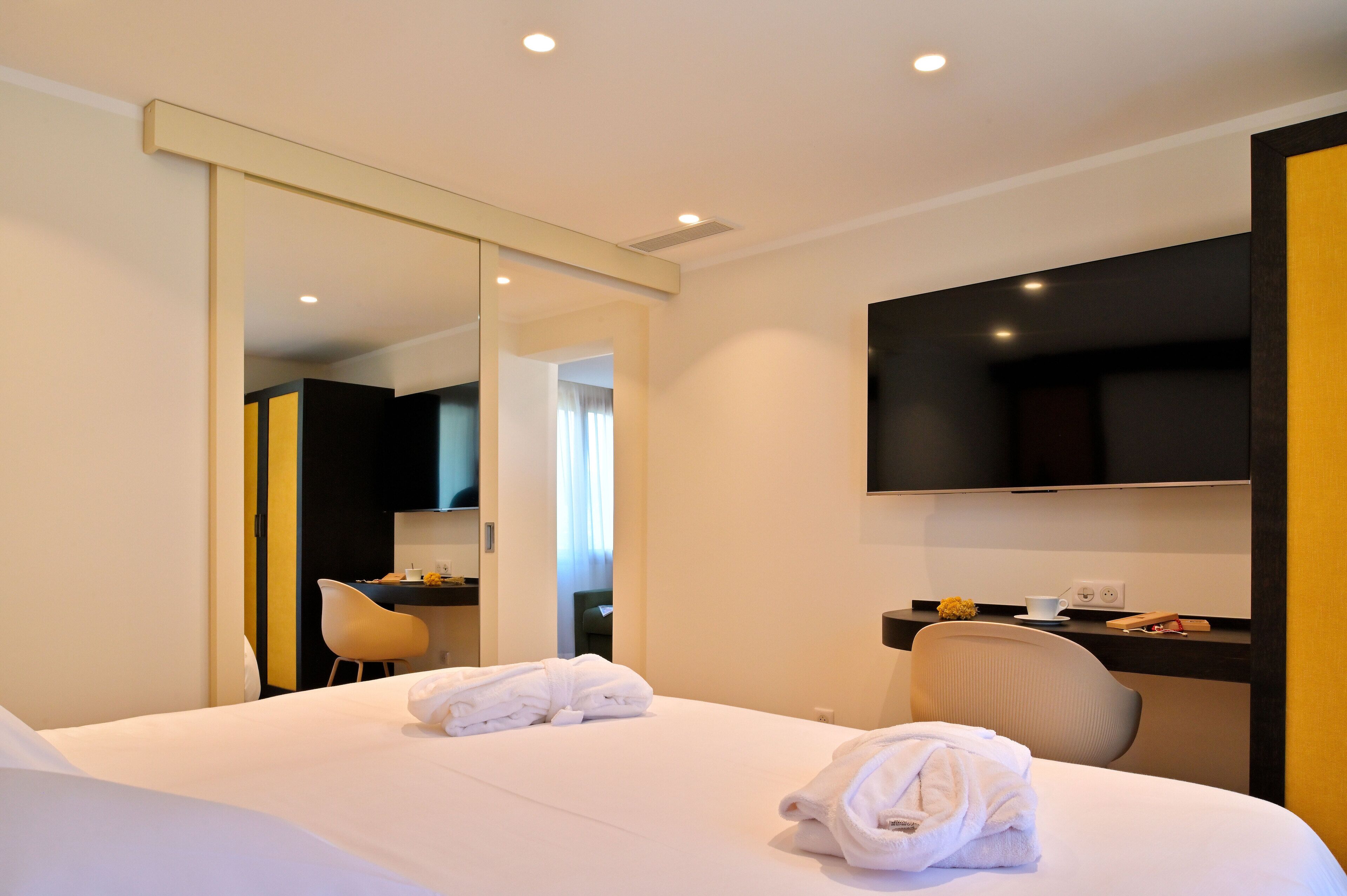A hotel room with a bed, a desk, a chair, and a large mirror.