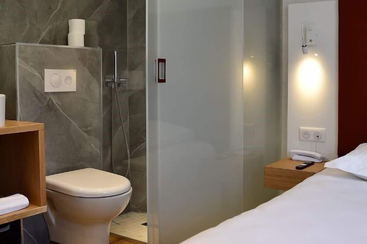Un baño moderno con cabina de ducha de vidrio, un inodoro y una mesita de noche con un teléfono.